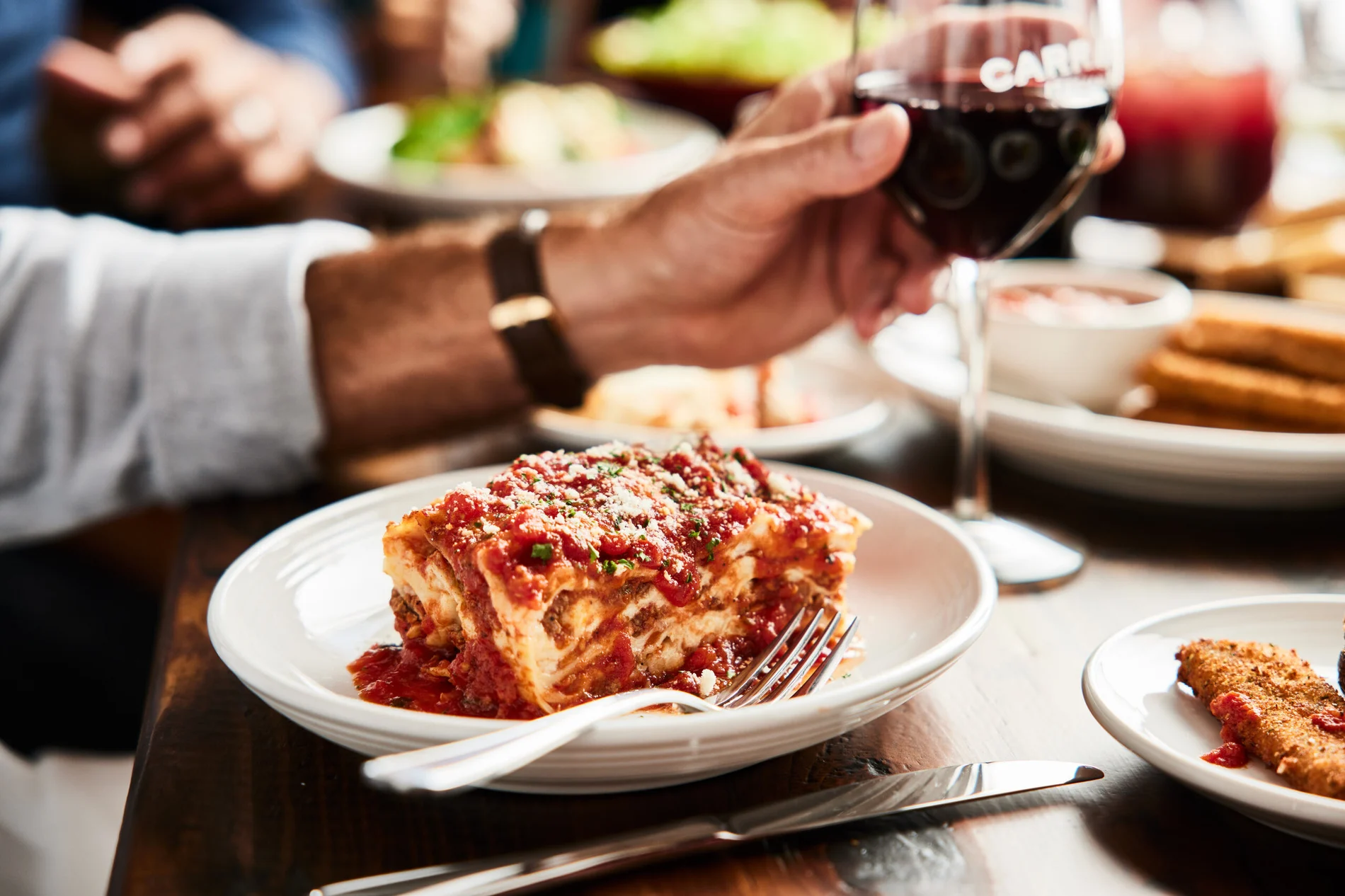 Man raising a glass of wine in a toast while enjoying lunch with others at an Italian restaurant in Greensboro NC.