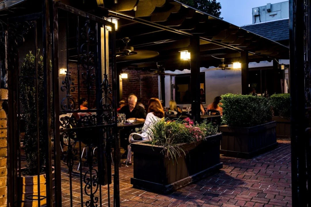 Outdoor restaurant patio with wooden tables, chairs, and potted plants under a clear blue sky