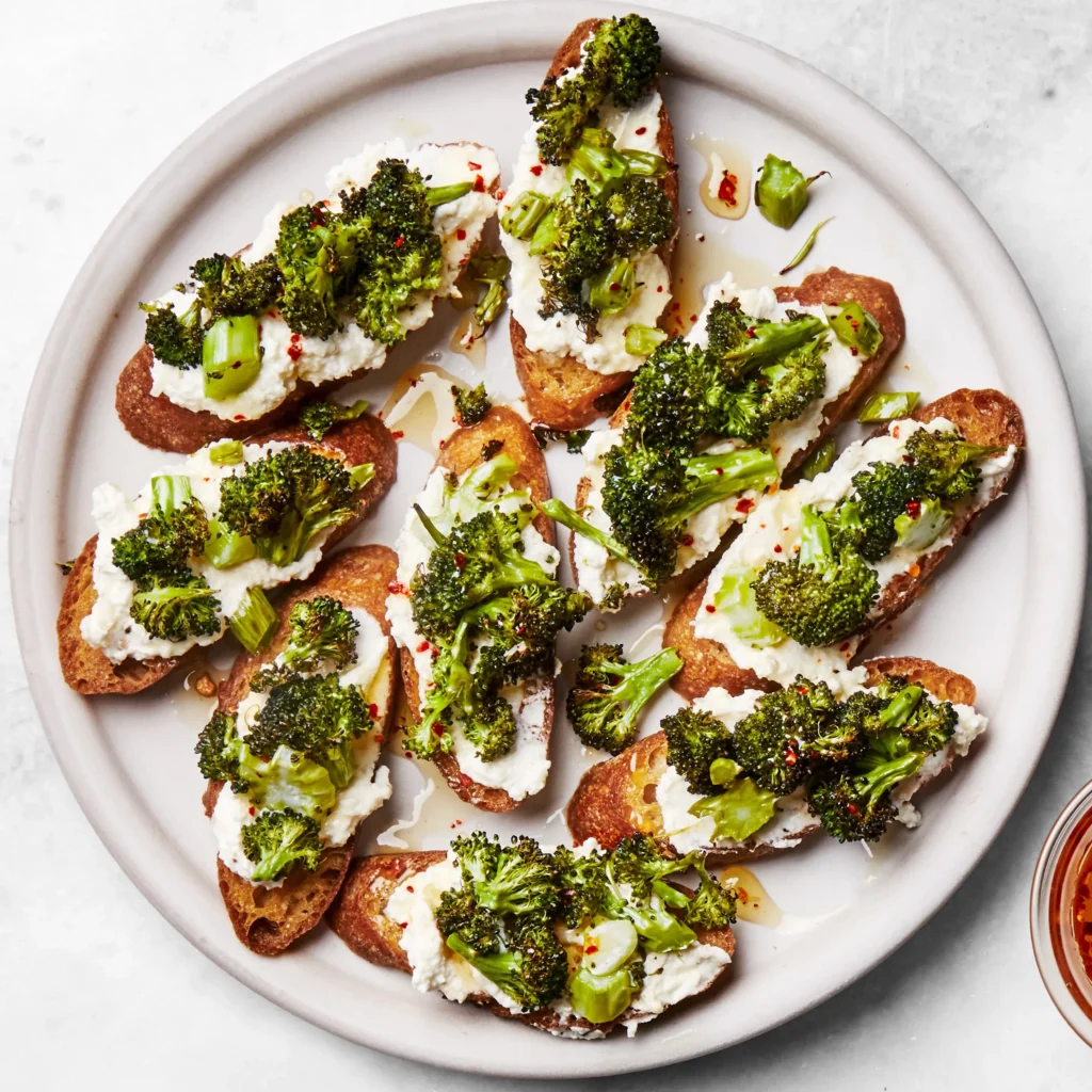 Toast appetizer topped with sautéed broccoli and goat cheese, garnished with fresh herbs