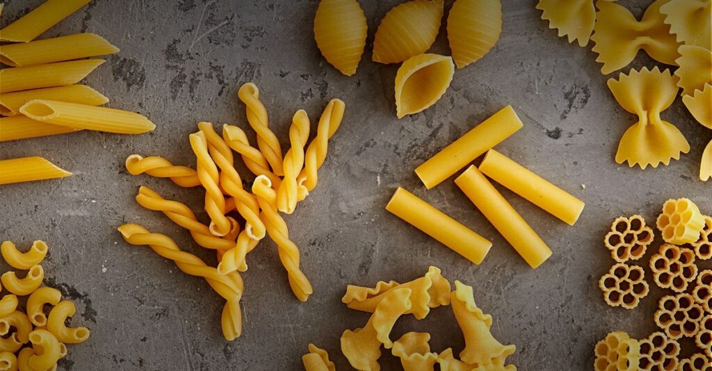 Variety of pasta including spaghetti, penne, and fusilli on a wooden table