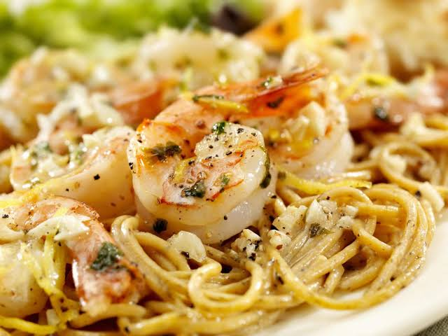 Shrimp scampi with pasta, lemon wedges, and fresh herbs on a plate